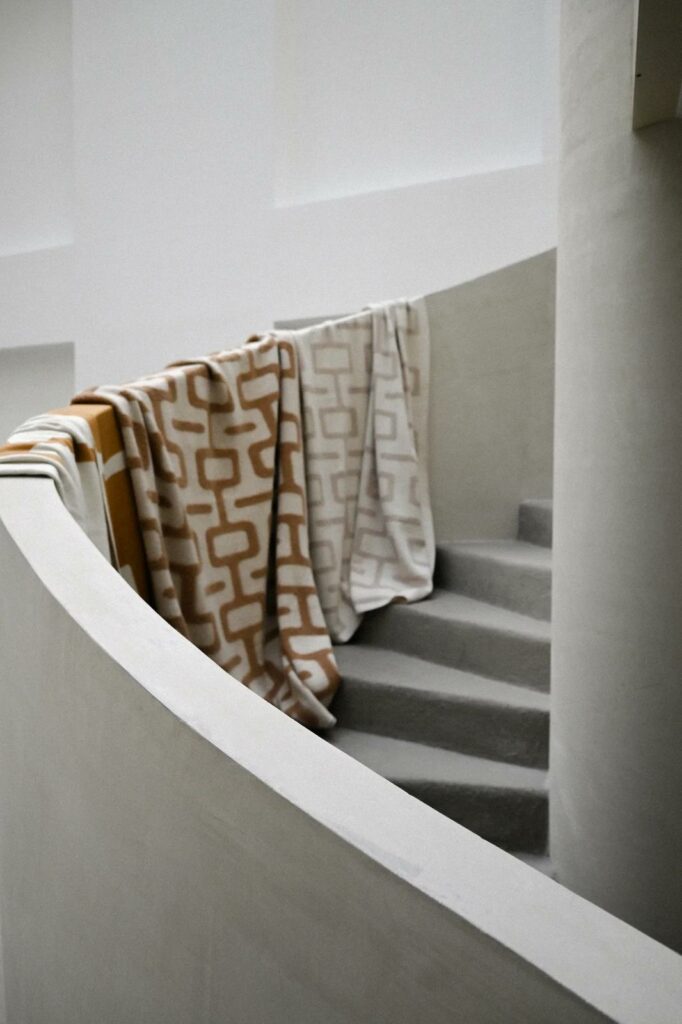Plaid en maille bouclette avec motif graphique disposé sur un escalier en béton, intégration textile dans un espace architectural
