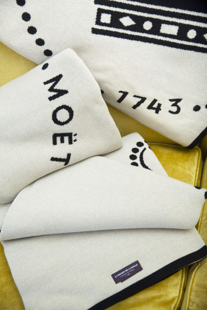 Détail du plaid en cachemire recyclé Moët & Chandon avec typographie et signature graphique, tricot d’exception