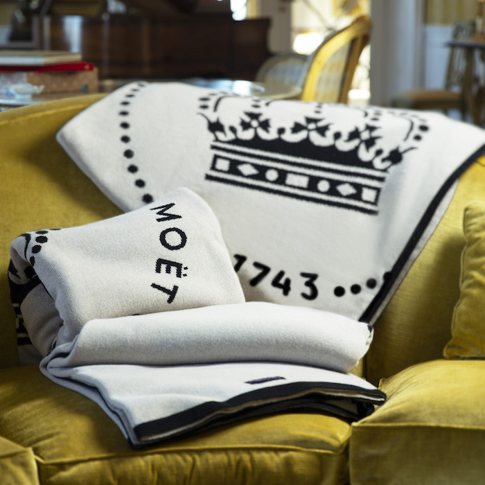 Plaid en laine cachemire recyclé Moët & Chandon disposé sur un canapé, pièce textile sur-mesure pour un intérieur haut de gamme