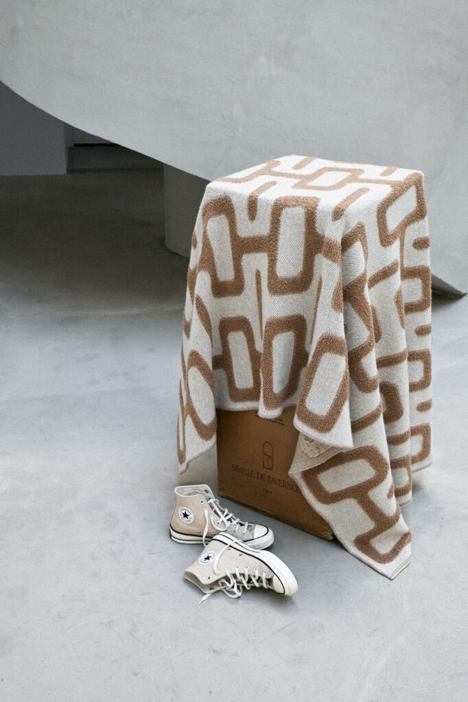 Plaid en maille bouclette avec motif géométrique drapé sur un volume, mettant en valeur la texture et le relief