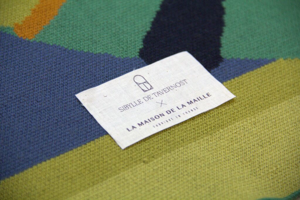 Détail d’un plaid en maille bouclette avec étiquette Sibylle de Tavernost et La Maison de la Maille